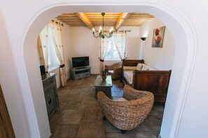 A living room with a television, wicker furniture, a chandelier, and a wooden ceiling. - Holiday home in Lioux with swimming pool (Lioux)