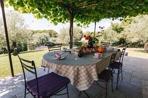 Un espace de restauration en plein air avec une table dressée pour deux personnes, entourée de chaises, sous un arbre.