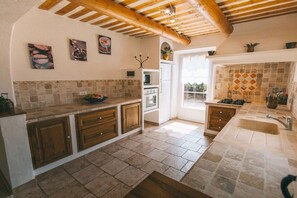 Une cuisine avec un sol carrelé en pierre, des meubles de rangement en bois, un four encastré et un pare-feu en carreaux.
