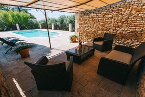 Une terrasse extérieure avec un mur en pierre, une piscine et du mobilier d’extérieur.