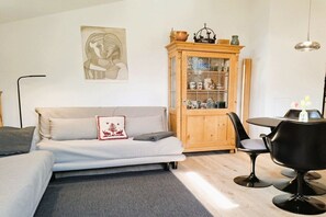 A modern living room with a sofa, a cabinet with glass doors, a dining table with chairs, and a painting on the wall. - Floor cutting suites summit view (Rottach-Egern)