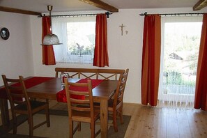 A dining area with a wooden table and chairs, red tablecloths, a hanging lamp, and a window with curtains. - Holiday apartment in Achslach with Wi-Fi (Achslach)