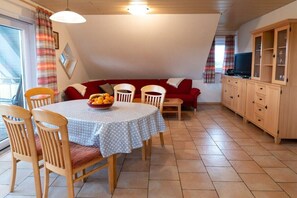 Un comedor con una mesa redonda, sillas, un frutero, un sofá rojo y un aparador de madera con puertas de cristal.