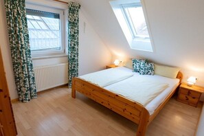 A bedroom with a wooden bed, two bedside tables, a window with curtains, a skylight, and a radiator. - Holiday apartment with 1 bedroom (Tettnang)