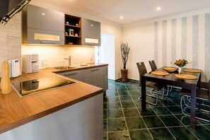 A modern kitchen with a built-in oven, a sink, and a dining area with a table and chairs. - Small and charming terraced house (Kühlungsborn)