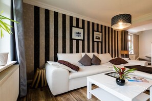 A modern living room with a striped wall, a white sofa, a coffee table, and a hanging light fixture. - Small and charming terraced house (Kühlungsborn)