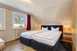 A bedroom with two beds, a window with a view, a radiator, and bedside lamps. - Holiday apartment with 1 bedroom (Seebad Ahlbeck)