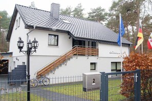 A white building with a tiled roof, a wooden staircase, and a metal gate with a number sign. - Holiday apartment with 1 bedroom (Seebad Ahlbeck)