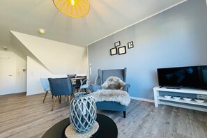 A modern living room with a dining area, a television, and a staircase. - ||----------------------Beachcomber F4---------------------|| (Norderney)