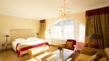 Ein Hotelzimmer mit einem Bett, einer Sitzecke mit Sofa und Sesseln, einem Couchtisch und einem großen Fenster mit Vorhängen.