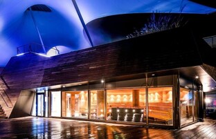 A modern building with a curved roof, large windows, and a wooden deck.