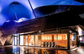 A modern building with a curved roof, large windows, and a wooden deck. - Moknis Palais Hotel and Spa (Bad Wildbad)