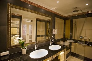 A bathroom with two sinks, a large mirror, a shower, and a towel rack. - Moknis Palais Hotel and Spa (Bad Wildbad)