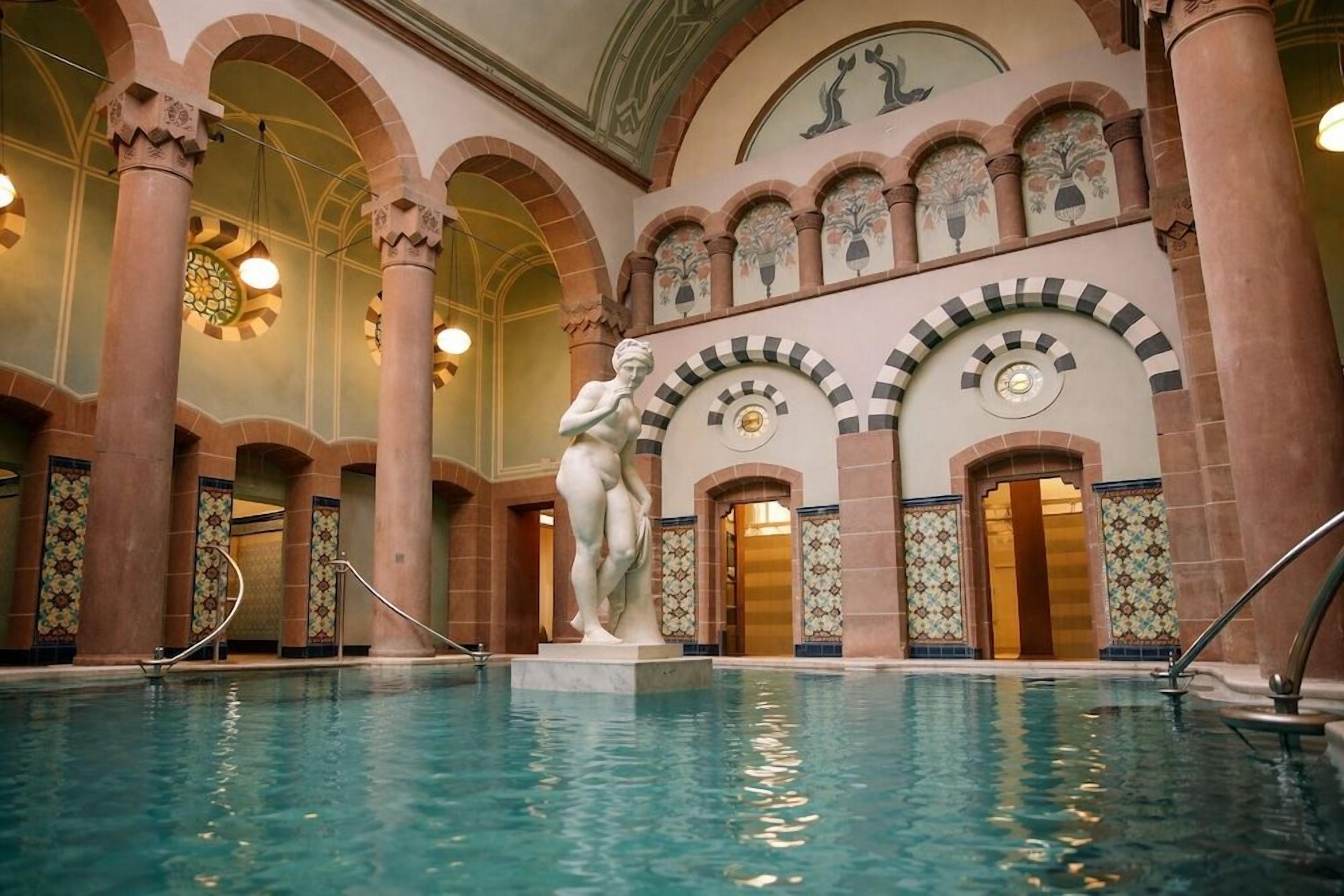 Ein Innenpool mit einer klassischen Statue, Rundsäulen und dekorativen Fliesen.