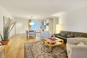 A modern living room with a sofa, a coffee table, and a dining area with chairs. - Holiday apartment with 2 bedrooms (Seebad Heringsdorf)