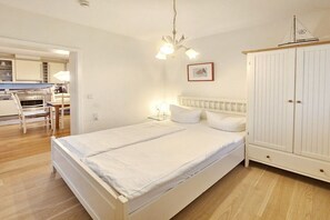 A bedroom with a bed, bedside table, lamp, wardrobe, and a view into the adjacent room. - Holiday apartment with 2 bedrooms (Seebad Heringsdorf)