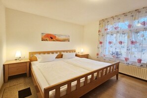Un dormitori amb un llit de fusta, dues taules de nit amb làmpades, cortines florals i un quadre a la paret.