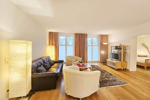 A modern living room with a sofa, armchair, TV stand, and a lamp. - Holiday apartment with 2 bedrooms (Seebad Heringsdorf)