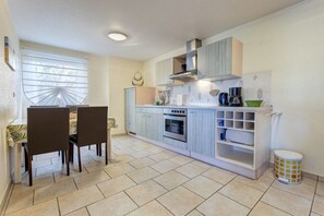 A compact kitchen with a dining area, featuring a stove, oven, and built-in shelves. - Villa "Helma" Apartment 1 (Seebad Heringsdorf)