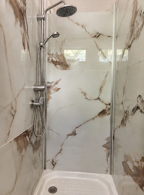 A shower enclosure with a glass door, a handheld showerhead, and a wall-mounted showerhead. - Patio & tropical garden, BBQ, 5 minutes from the beach (Rivière-Pilote)