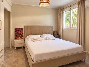 A hotel room with a bed, bedside table, and a painting. - Patio & tropical garden, BBQ, 5 minutes from the beach (Rivière-Pilote)