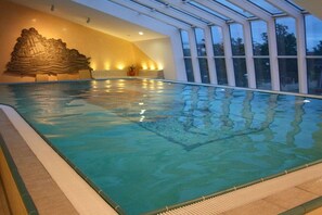 An indoor swimming pool with clear water, a stone wall sculpture, and large windows. - "Sea View" Trafalgar (Cuxhaven, Deutschland)