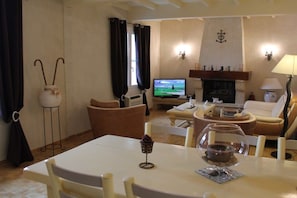 A living room with a television, a fireplace, a dining table, and a sofa. - Holiday home in Maillane with swimming pool (Maillane)