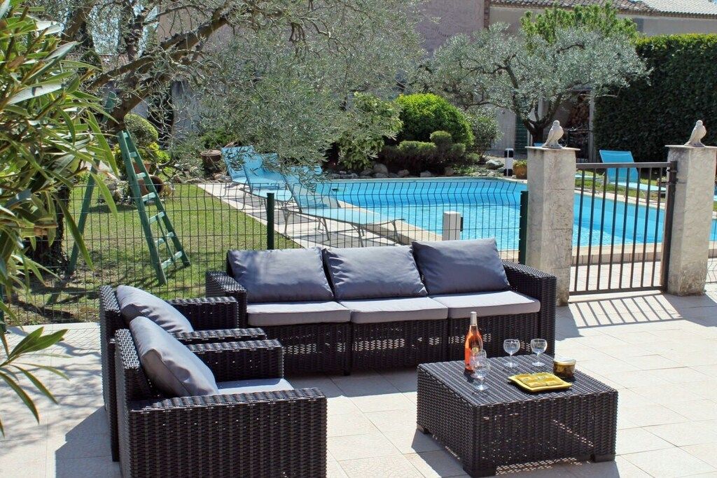 Un espace aménagé au bord de la piscine, avec un canapé en osier et une table basse, entouré de verdure et offrant une vue sur la piscine.