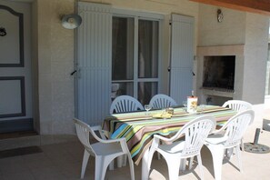 An outdoor dining area with a table set for four, surrounded by white chairs, under a covered patio. - Holiday home in Maillane with swimming pool (Maillane)