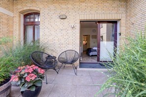 A brick building with a door leading to a room, two chairs outside, and potted plants. - Holiday apartment with 1 bedroom (St. Peter-Ording)