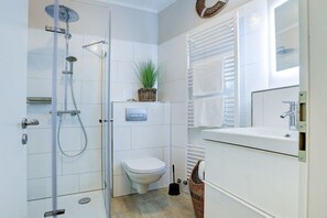 A modern bathroom with a glass-enclosed shower, a toilet, and a sink with a mirror. - Holiday apartment with 1 bedroom (St. Peter-Ording)