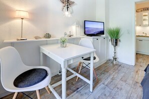 A compact living space with a dining table, two chairs, a television, and a potted plant. - Holiday apartment with 1 bedroom (St. Peter-Ording)