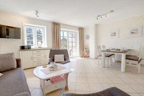 A spacious living area with a sofa, a dining table set for four, and a kitchen area with cabinets and a microwave. - Ordinger Dün Holiday Apartment 2 (St. Peter-Ording)