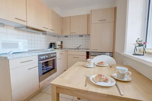 A modern kitchen with a microwave, oven, and dining table set with croissants and cups. - Ordinger Dün Holiday Apartment 2 (St. Peter-Ording)
