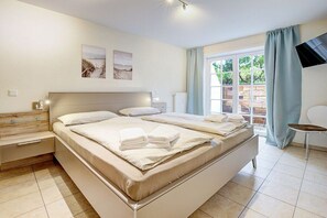 A bedroom with a large bed, bedside tables, a TV, and a window with curtains. - Ordinger Dün Holiday Apartment 2 (St. Peter-Ording)