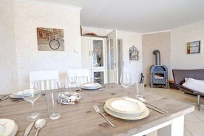 A dining area with a wooden table set for four, a fireplace, and a sofa in the background. - Ordinger Dün Holiday Apartment 2 (St. Peter-Ording)