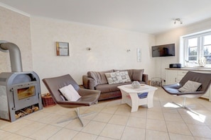 A living room with a fireplace, a sofa, two chairs, a coffee table, and a television. - Ordinger Dün Holiday Apartment 2 (St. Peter-Ording)