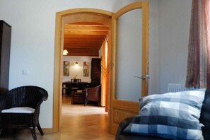 Een kamer met een bed, een stoel en een houten deur die naar een andere kamer leidt.
