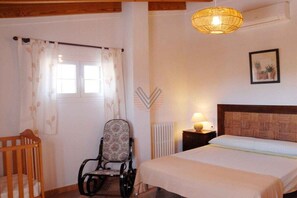 A bedroom with a bed, a chair, a radiator, and a window with curtains. - Finca Tugores [1970A] (Lloseta)