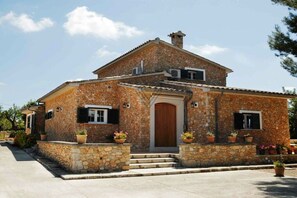 A stone house with a wooden door, potted plants, and a clear sky. - Finca Tugores [1970A] (Lloseta)