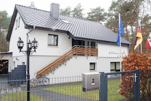 A white building with a tiled roof, a wooden staircase, and a metal gate with a number sign. - Holiday apartment with 2 bedrooms (Seebad Ahlbeck)