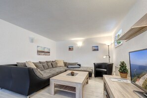 A modern living room with a sectional sofa, a coffee table, a black armchair, a desk with a computer, and a large TV screen. - Holiday apartment with 2 bedrooms (Seebad Ahlbeck)