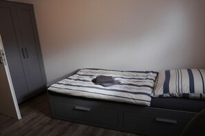 A bedroom with a bed, a wardrobe, and a small drawer unit. - Holiday home on the North Sea coast? (Wittmund)