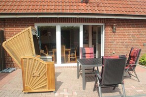 Eine Terrasse mit Tisch und Stühlen, ein Korbstuhl und ein Backsteinhaus mit Ziegeldach.