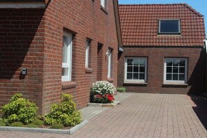 Ein rot backengebackenes Gebäude mit einem Ziegeldach, ein kleiner Garten mit Blumen und ein gepflasterter Weg.
