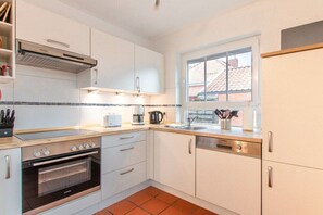 A modern kitchen with white cabinets, a built-in oven, a coffee maker, and a window providing natural light. - Holiday apartment with 1 bedroom (Norddeich)