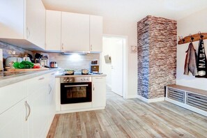 A modern kitchen with white cabinets, a built-in oven, and a stone accent wall. - Villa by the sea Apartment 4 (St. Peter-Ording)