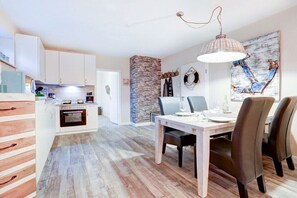 A modern kitchen with white cabinets, a stone accent wall, and a dining area with a wooden table and chairs. - Villa by the sea Apartment 4 (St. Peter-Ording)