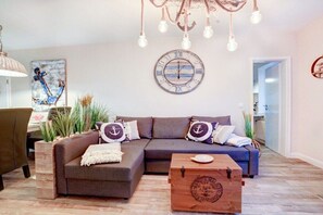 Een woonkamer met een hoekbank, een houten salontafel, een klok en een kroonluchter.