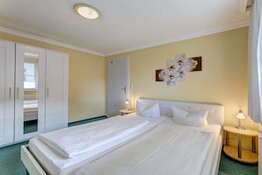 A hotel room with a double bed, a wardrobe, a bedside table with a lamp, and a wall-mounted artwork. - Villa "Helma" Apartment 2 (Seebad Heringsdorf)